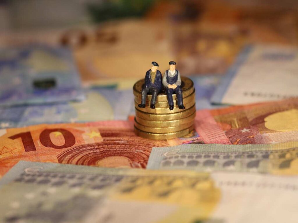 statuine che raffigurano due anziani seduti sopra una pila di monete circondati da banconote